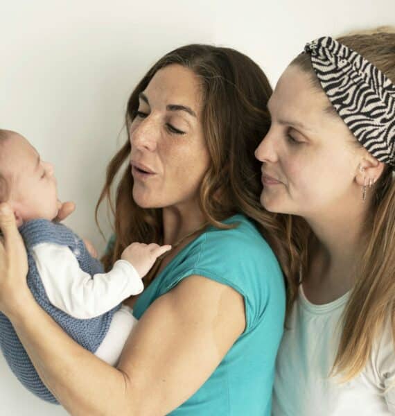 Deux femmes admirant un bébé que l'une d'elles tient dans ses bras, avec des expressions d'affection et de joie, près du Cabinet Doré-Onrozat.
